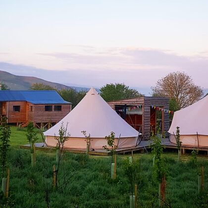 A photograph of two bell tents with a log cabin and hills in the background