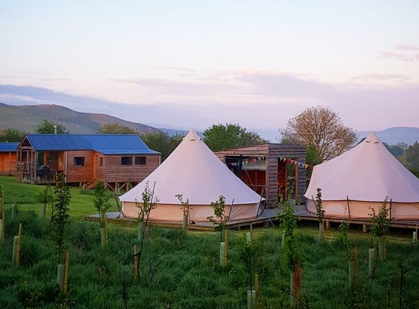 A photograph of two bell tents with a log cabin and hills in the background