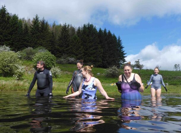 A photograph of a group of men and women entering a lake to go wild swimming.