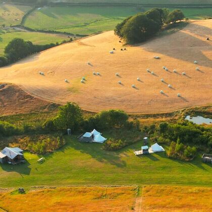 An aerial photograph of a glamping retreat venue with five bell tents and a large log cabin