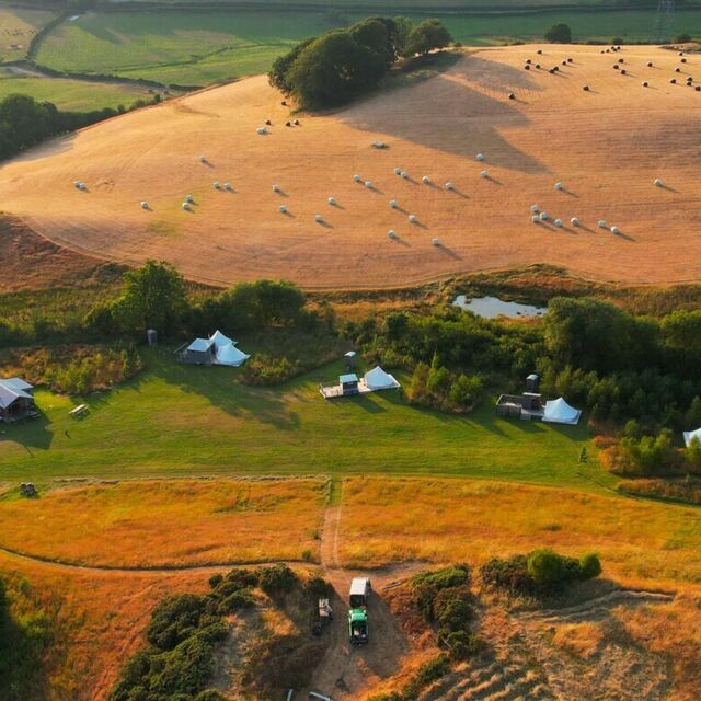 An aerial photograph of a glamping retreat venue with five bell tents and a large log cabin beside a hill fort