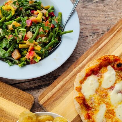 A photograph of a pizza with a bowl of crisps and a green bean and beetroot salad