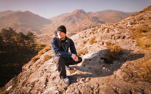 A man in winter walking gear crouching on a rocky outcrop in the Welsh mountains.