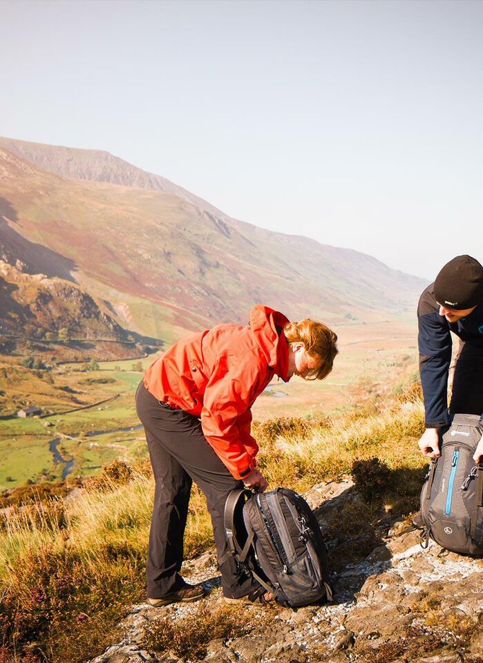 A young couple hiking in the Welsh mountains, arranging their backpacks.