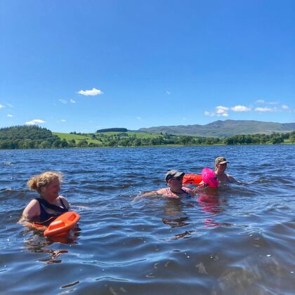 A photo of three ladies swimming in a lake with a mountain in the background