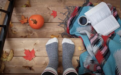 A photograph of a person wearing cosy socks with a book, a cup of coffee, a pumpkin and a warm  blanket.