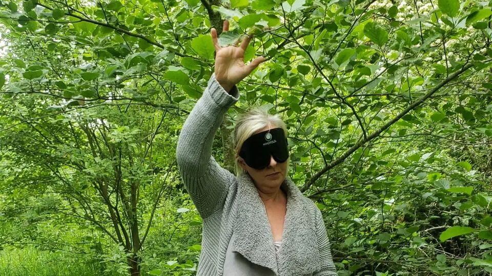 A blindfolded woman using a rope to move through a woodland