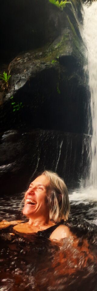 A photograph of a woman in a waterfall with a look of pure joy and happiness on her face.