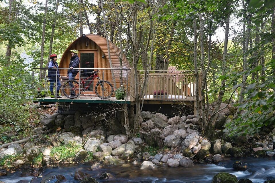A  photograph of a glamping pod in a forest with a man on a bicycle in the foreground