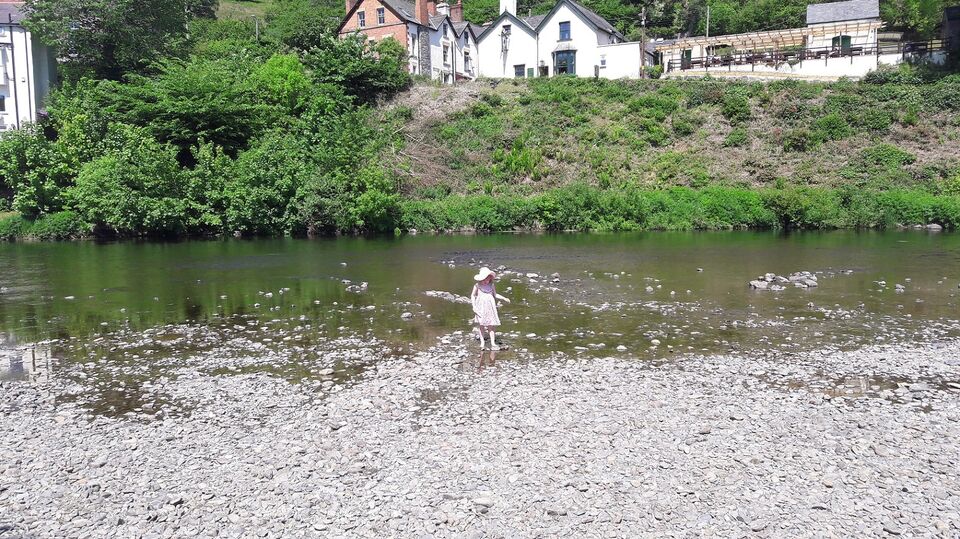 A photograph of a little girl paddling in a river in front of a pub