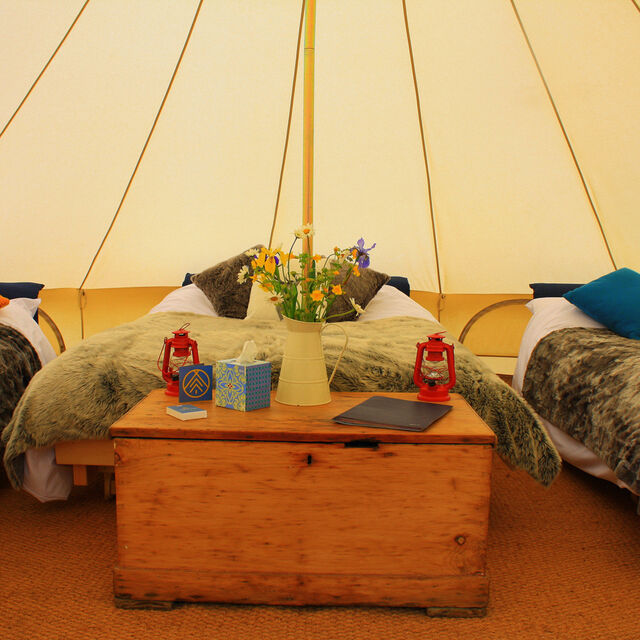 A photograph of the inside of a bell tent showing three beds, cosy throws and red lanterns