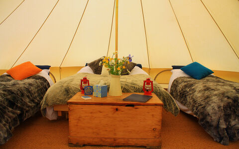 A photograph of the inside of a bell tent showing three beds, cosy throws and red lanterns