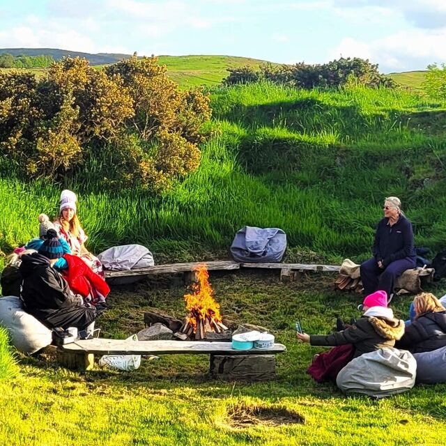 A photograph of a group of ladies sitting around a campfire