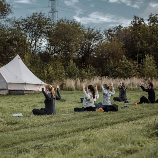 A photograph of a group of people doing yoga outdoors in front of a bell tent