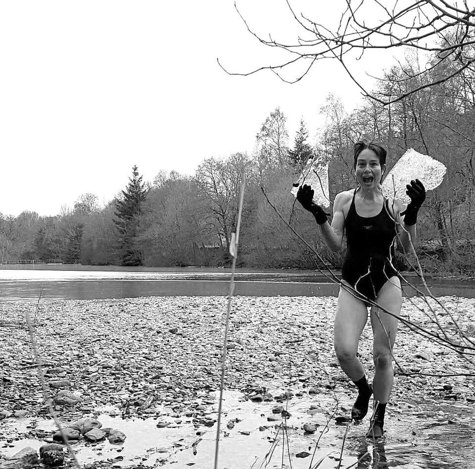 A photograph of a lady emerging from a frozen lake holding two large blocks of ice in her hands