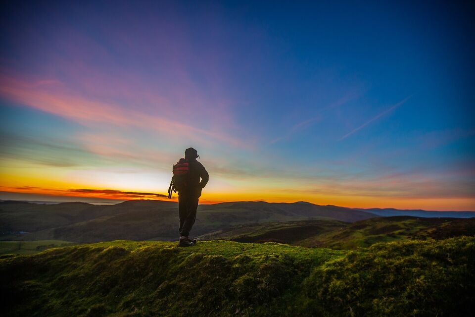 A photograph of a man walking on a hill at sunset