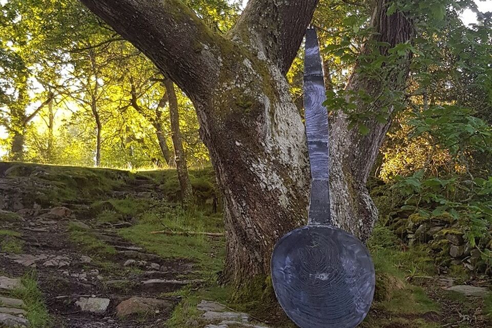 A photograph of a giant spoon leaning against a tree in a wood