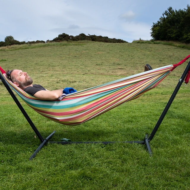 A photograph of a man in a hammock with a hill fort in the background