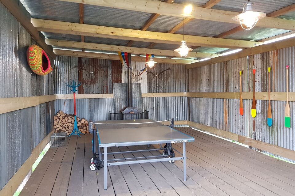 A photograph of a tin hut with a ping pong table and a log burner