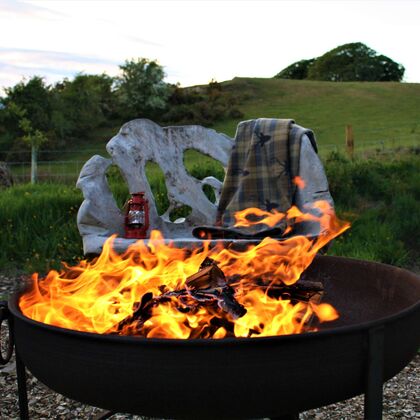 A photo of a log fire in a fire bowl with a blanket and a red lantern on the bench in the background