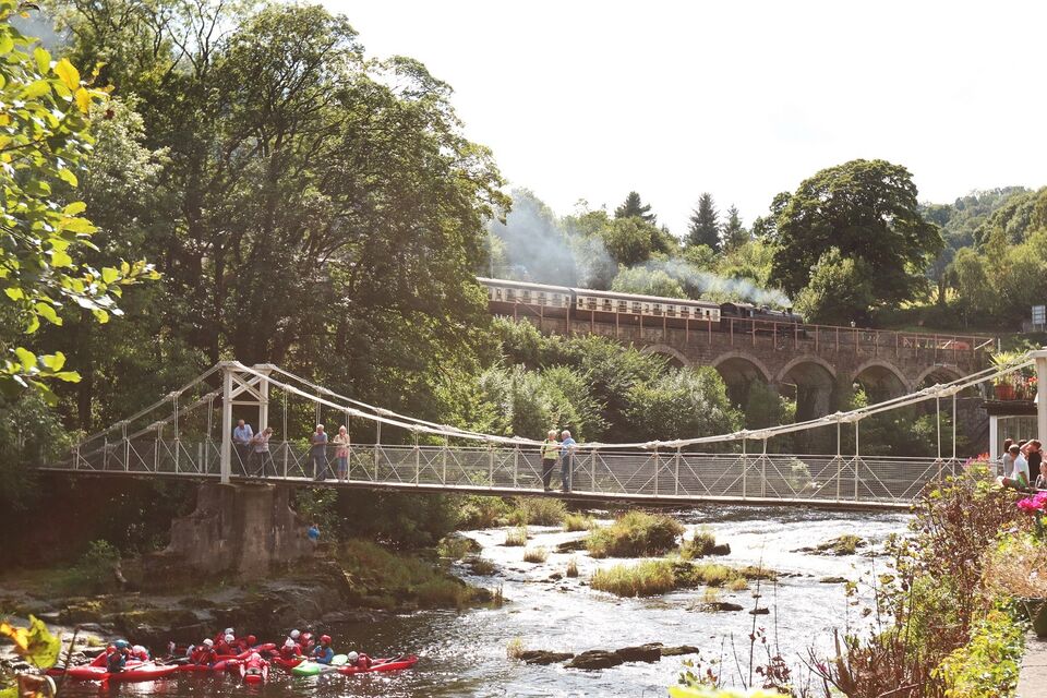 A photograph of chain bridge with a steam train in the background